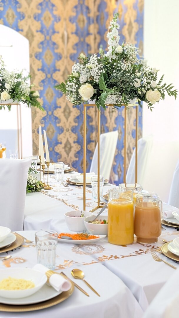 Elegancko nakryty stół komunijny w Rezydencji Dwór Górny w Nowej Rudzie, złote dekoracje, białe kwiaty i zabytkowa sala z niebiesko złotą tapetę.