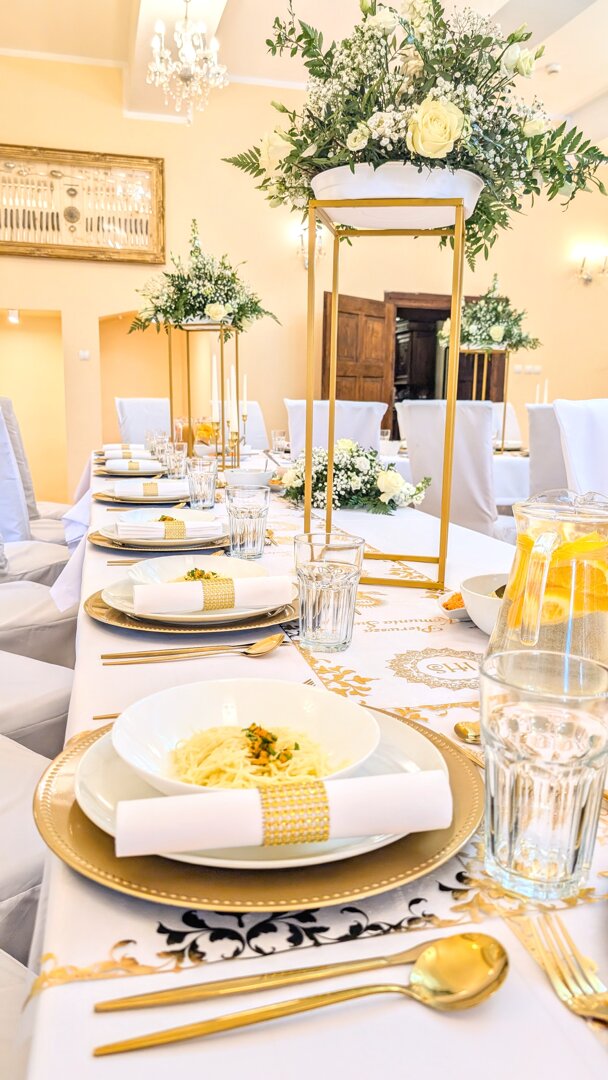 Obiad komunijny w Nowej Rudzie: luksusowa zastawa ze złotymi sztućcami, serwetki z cyrkoniami, złote podtalerze, białe kwiaty na wysokich stojakach i zabytkowe wnętrza dworu. W tle odnaleziony skarb - zabytkowa srebrna zastawa.